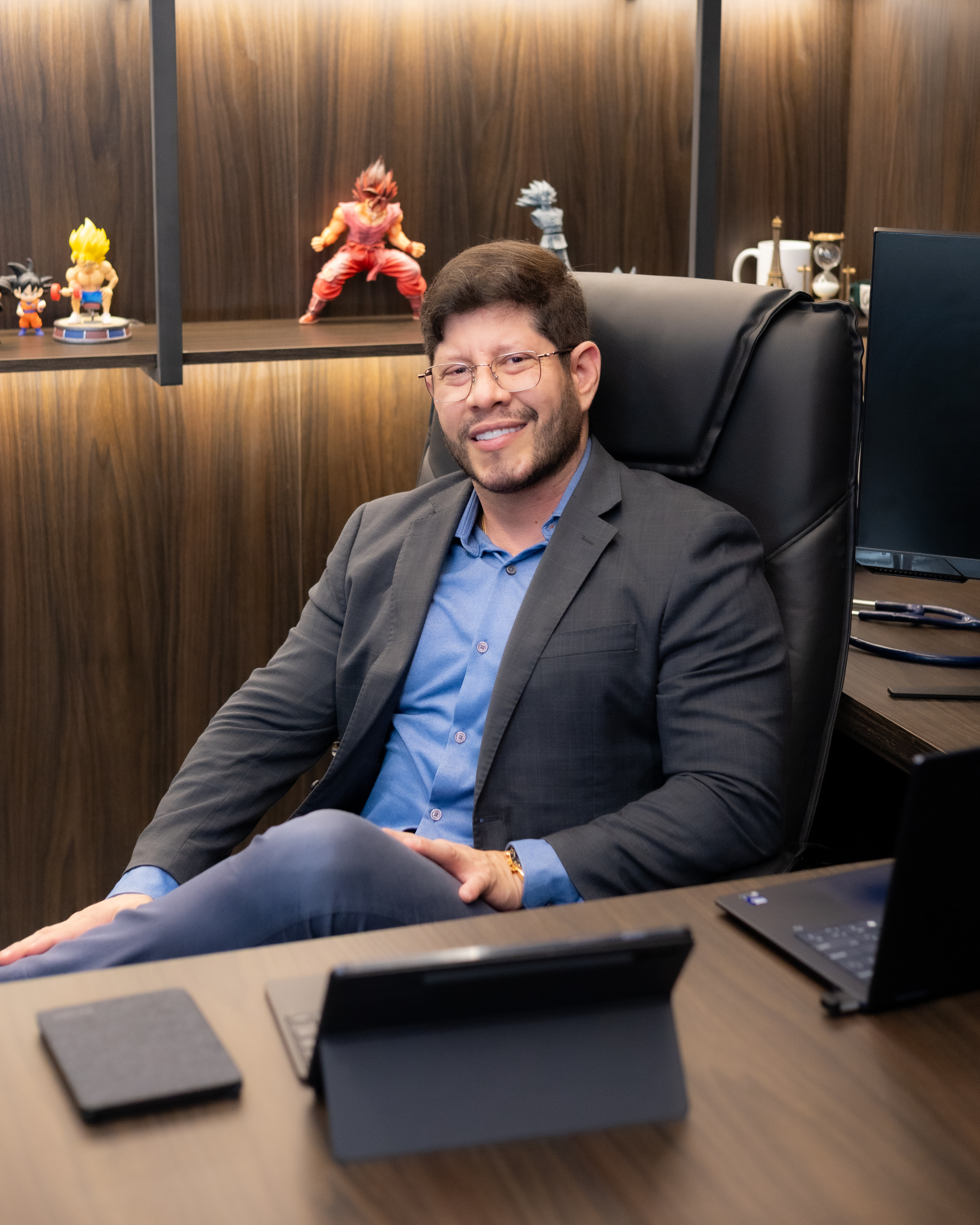 Dr. André Nascimento sentado em seu consultório, sorrindo e usando blazer